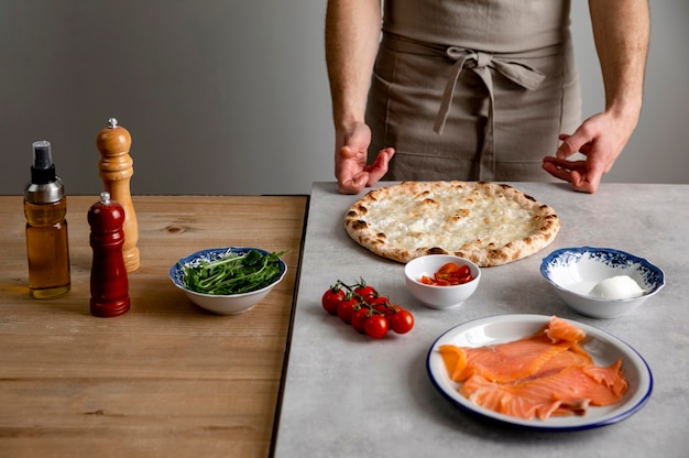 Mens die zich dichtbij gebakken pizzadeeg en ingrediënten bevindt