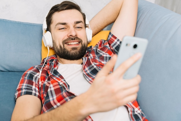 Mens in hoofdtelefoons die smartphone gebruiken