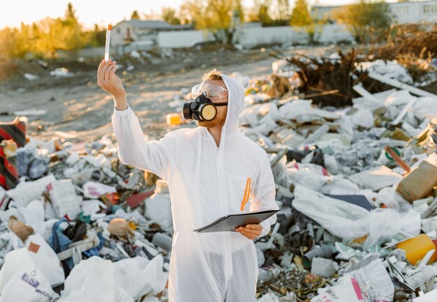 Mens in overall bij prullenbakpil. Onderzoek doen. Concept van ecologie, milieuvervuiling.