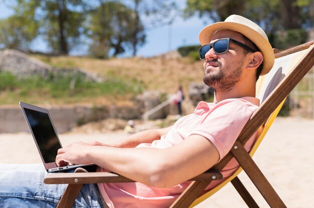 Mens in strandstoel die aan laptop werkt