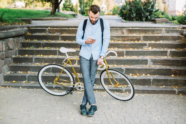 Mens met fiets die smartphone gebruiken dichtbij treden