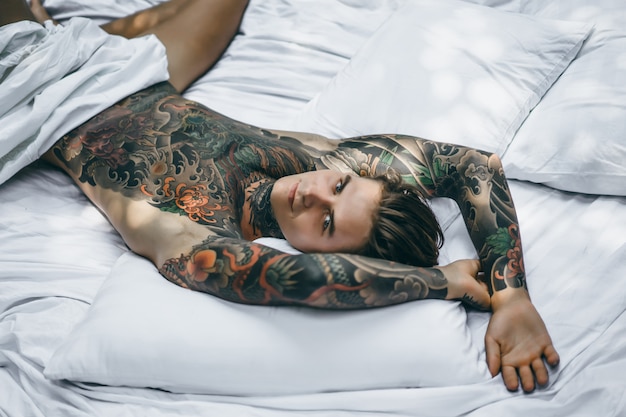 Gratis foto mens met kleurrijke tatoegeringen die op een wit blad stellen