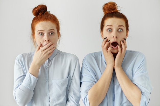 Menselijke emoties en gevoelens. Gezichtsuitdrukkingen. Twee roodharige verbaasde blanke studenten die eruit zagen als een tweeling met haarknopen gekleed in overhemden. Zusjes met insectenogen leerden schokkende informatie