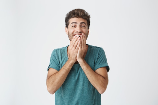 Menselijke gezichtsuitdrukkingen, emoties en gevoelens. Verbaasd en verrast bebaarde jonge man in blauw t-shirt wijzend op blinde muur, vertellen dat hij een idee heeft