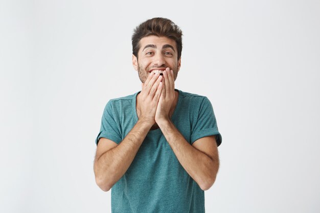 Menselijke gezichtsuitdrukkingen, emoties en gevoelens. Verbaasd en verrast bebaarde jonge man in blauw t-shirt wijzend op blinde muur, vertellen dat hij een idee heeft