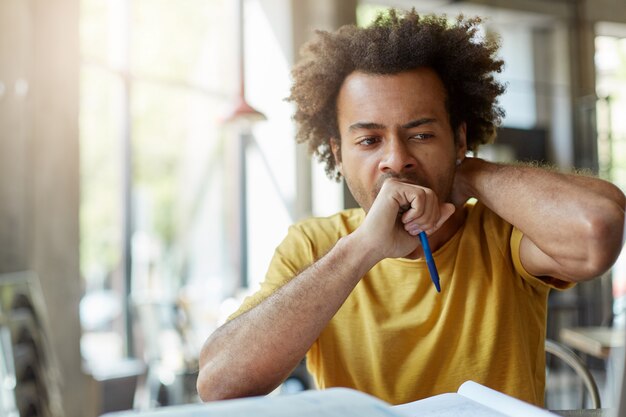 Menselijke gezichtsuitdrukkingen, emoties, gevoelens en houding. Moe, slaperig Afro-Amerikaanse student die geopende mond met vuist bedekt terwijl geeuwen, zittend aan een bureau met boeken, voorbereiden op onderzoek