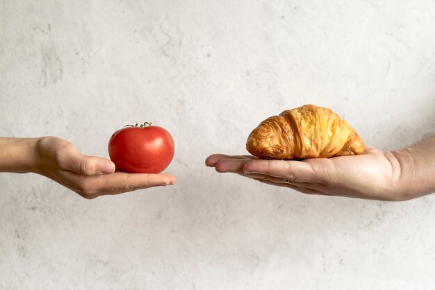 Menselijke hand die croissant en rode tomaat voor concrete achtergrond toont