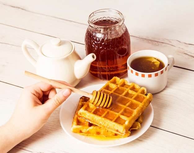 Menselijke hand gietende honing op Belgische wafels die honingsdipper gebruiken