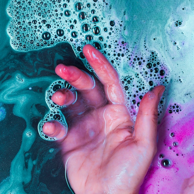 Gratis foto menselijke hand in blauwe vloeistof met schuim en vlekken