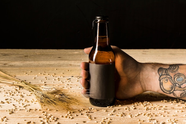 Menselijke hand met alcoholische fles met oren van tarwe op houten oppervlak