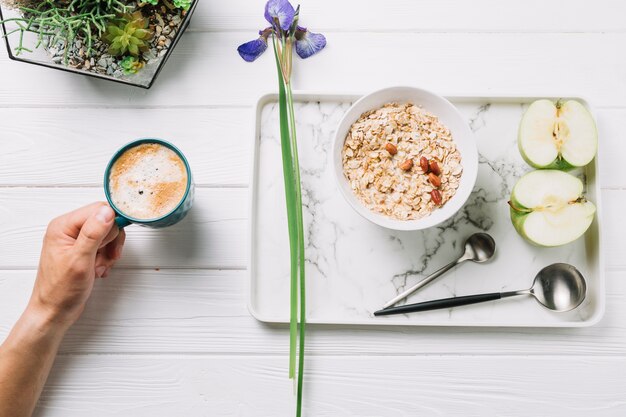 Menselijke hand met een kopje koffie met heerlijk ontbijt op houten plank