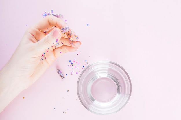 Menselijke hand met transparante capsule gevuld met confetti naast glas op water