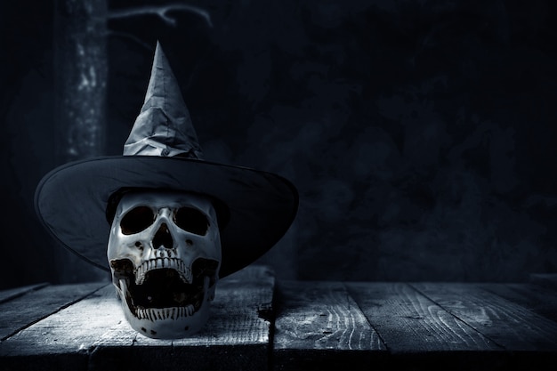 Menselijke schedel op houten tafel met een hoed op de donkere achtergrond