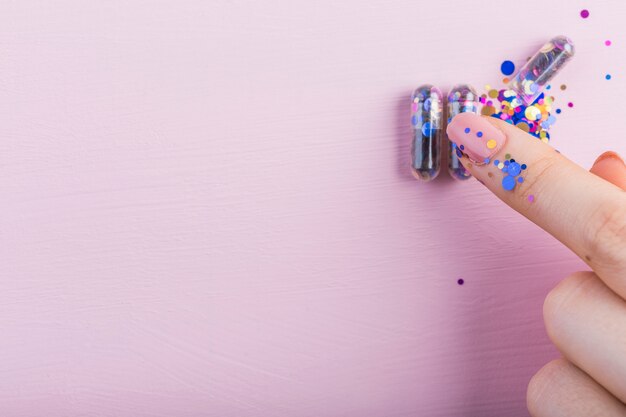 Menselijke vinger wat betreft lovertjescapsule op roze achtergrond