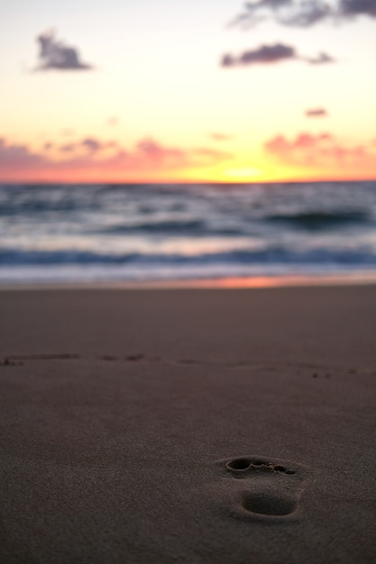 Menselijke voetafdruk op het zandstrand dat glanst onder de zonsondergang