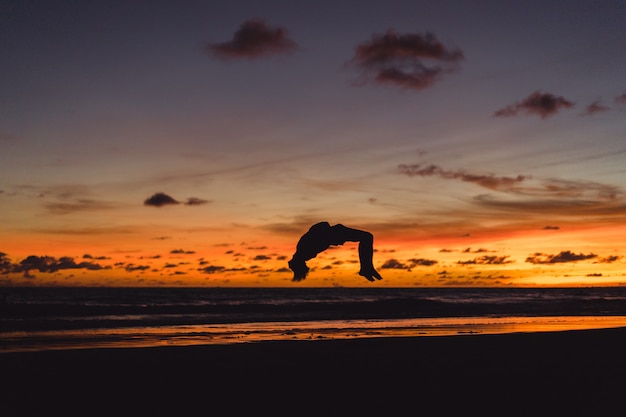 mensen aan de oever van de Oceaan bij zonsondergang. man springt tegen de achtergrond van de ondergaande zon