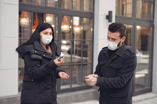 Mensen die een beschermend masker dragen dat zich op straat bevindt terwijl ze alcoholgel gebruiken