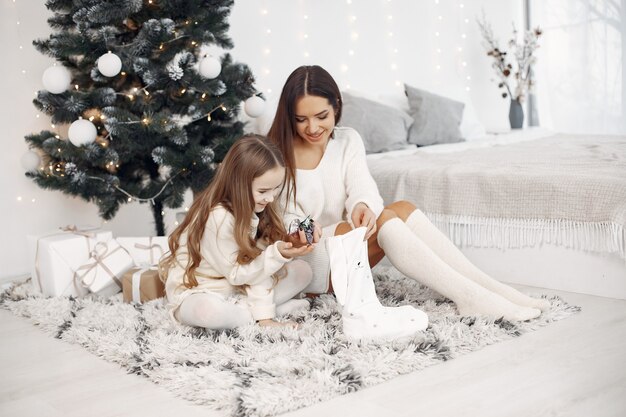 Mensen die voor Kerstmis herstellen. Moeder speelt met haar dochter. Familie zit bij de kerstboom. Klein meisje in een witte jurk.