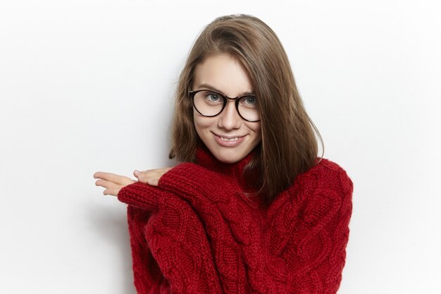 Mensen en levensstijlconcept. Foto van prachtige modieuze jonge blanke vrouw met losse haren poseren, het dragen van gebreide kastanjebruine pullover met lange mouwen, met mysterieuze look