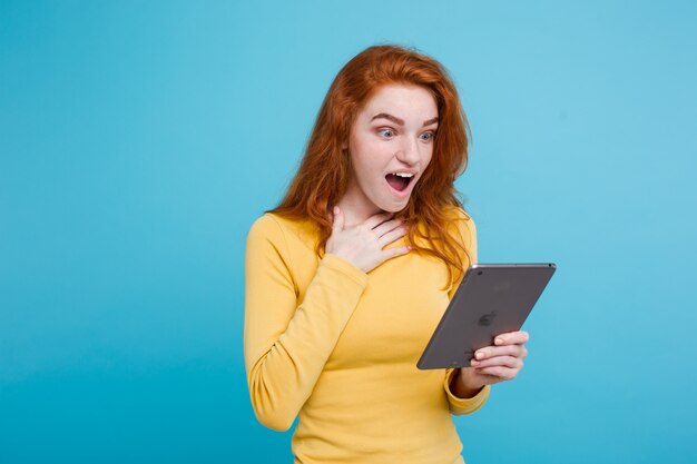 Mensen en technologie concept - close-up Portret jonge mooie aantrekkelijke roodharige meisje blij lachend op digitale tafel met wining iets. Blauwe Pastelachtergrond. Kopieer de ruimte.