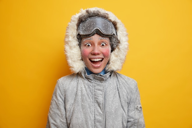 Mensen levensstijl en winteractiviteiten concept. vrolijke donkere vrouw glimlacht breed staat vol geluk draagt winterjas en skibril.