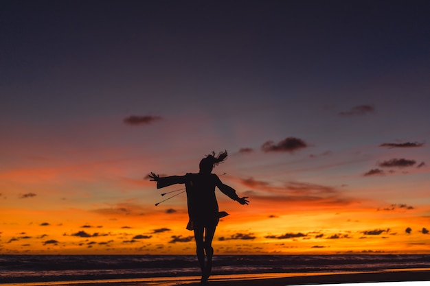 mensen op het strand bij zonsondergang. het meisje springt tegen de achtergrond van de ondergaande zon.