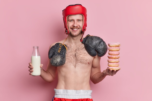 Mensen sport en voeding concept. Positieve magere mannelijke bokser poseert met naakte torso-glimlachen heeft graag de verleiding om donuts te eten en melk te drinken