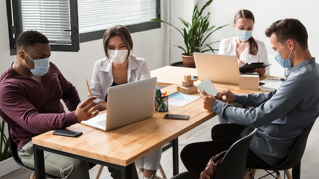 Mensen tijdens pandemie werken samen op kantoor met maskers op