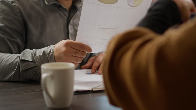 Mensen uit het bedrijfsleven analyseren onderzoeksinformatie over documenten, kijken naar papieren met tariefgrafieken en grafieken. Kantoormedewerkers die werken met infographics rapporteren en beoordelen. Detailopname.