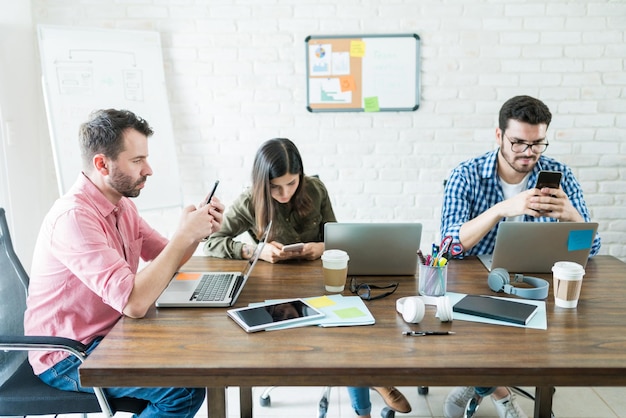 Mensen uit het bedrijfsleven zitten rond de vergadertafel terwijl ze socializen op mobiele telefoons op kantoor