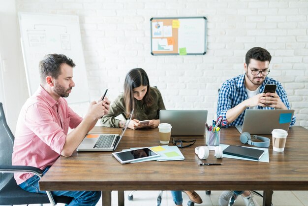 Mensen uit het bedrijfsleven zitten rond de vergadertafel terwijl ze socializen op mobiele telefoons op kantoor