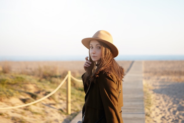 Mensen, vrije tijd, levensstijl en reizen. Gelukkig en zorgeloos brunette vrouw wandelen langs de kust, haar losse haren aanraken en zich omdraaien, haasten naar de oceaan tijdens het reizen in het buitenland