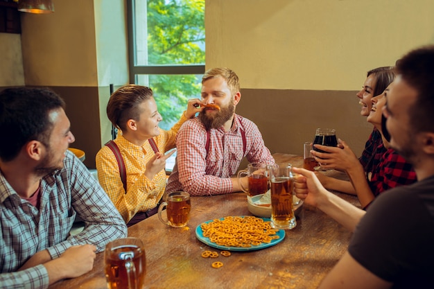 Mensen, vrije tijd, vriendschap en communicatieconcept - gelukkige vrienden die bier drinken, spreken en glazen klinken bij bar of bar