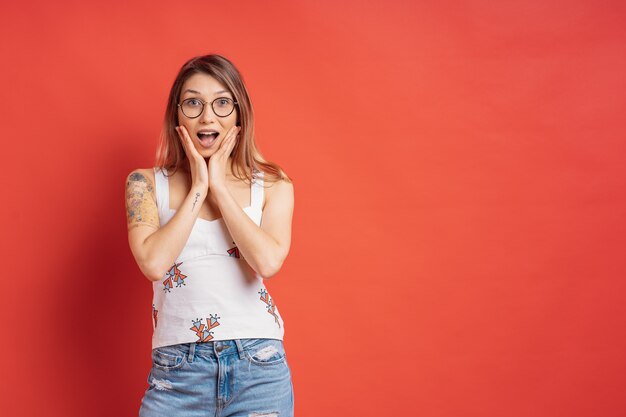 Mensenemoties - portret van verrast positief meisje over rode muur