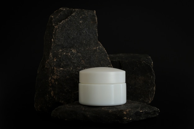 Merkloze natuurlijke cosmetische crèmeverpakking die op een stenen podium staat. crème presentatie op de zwarte achtergrond. mock-up. trending concept in natuurlijke materialen. natuurlijke cosmetica, huidverzorging.