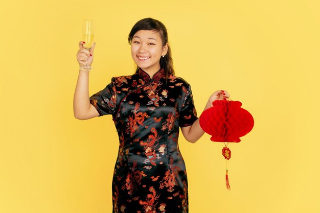 Met champagne en lantaarn. Gelukkig Chinees nieuwjaar. Aziatisch jong meisje portret op gele achtergrond. Vrouwelijk model in traditionele kleding ziet er gelukkig uit. Copyspace.