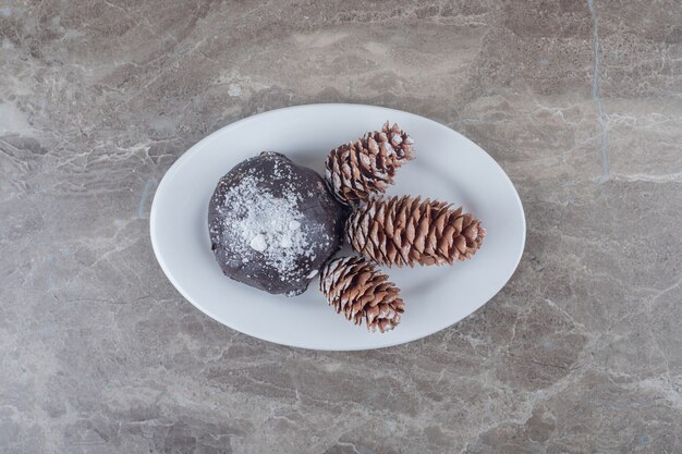 Met chocolade bedekte cake en drie dennenappels op een schotel op marmeren oppervlakc