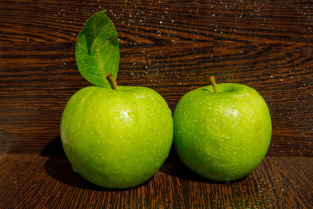 Met dauw bedekte groene appelen met blad op nat donker gebogen houten, zijaanzicht.