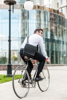 Met de fiets door de stad. achteraanzicht van een jonge zakenman die wegkijkt terwijl hij op zijn fiets rijdt