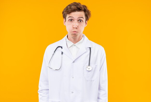 Met gepofte wangen jonge mannelijke arts die medisch gewaad draagt met stethoscoop
