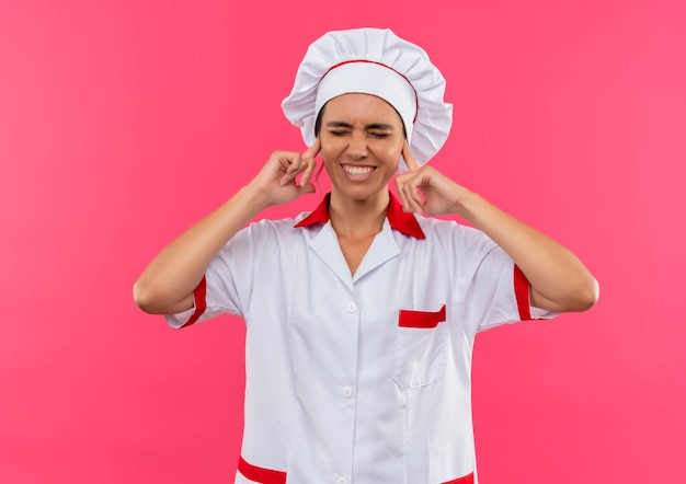 Met gesloten ogen glimlachende jonge vrouwelijke kok die chef-kok eenvormige gesloten oren met exemplaarruimte draagt