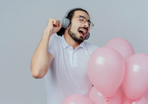 Met gesloten ogen vrolijke knappe man met bril houden ballonnen luisteren muziek op koptelefoon geïsoleerd op wit