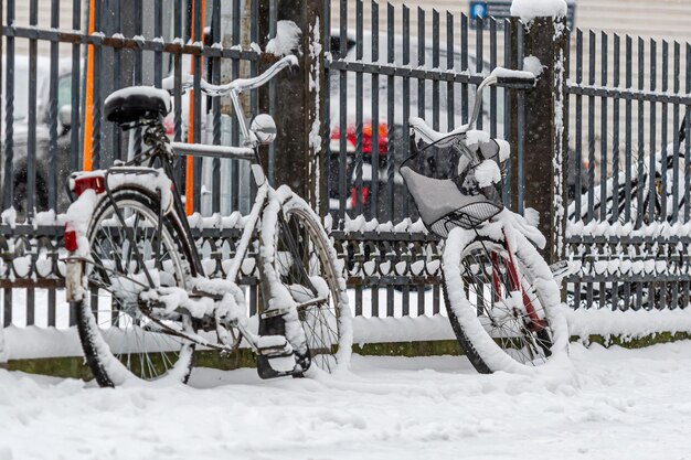 Met sneeuw bedekte fietsen worden geparkeerd en vergrendeld aan een hek op het trottoir in een winterse stad