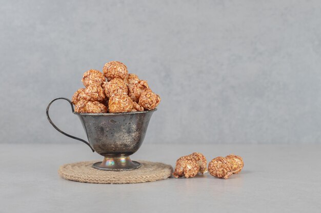 Metalen beker gevuld met bruine gekonfijte popcorn op marmeren tafel.