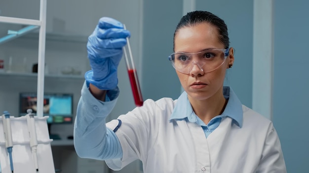 Microbiologie arts met reageerbuis gevuld met bloed in laboratorium op chemische dienblad. professionele vrouw die laboratoriumapparatuur draagt met behulp van glazen kolf en instrumenten voor onderzoeksontwikkeling