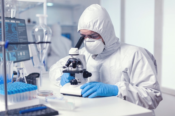 Gratis Foto microbioloog met beschermingsbril met microscoop gekleed pbm-pak