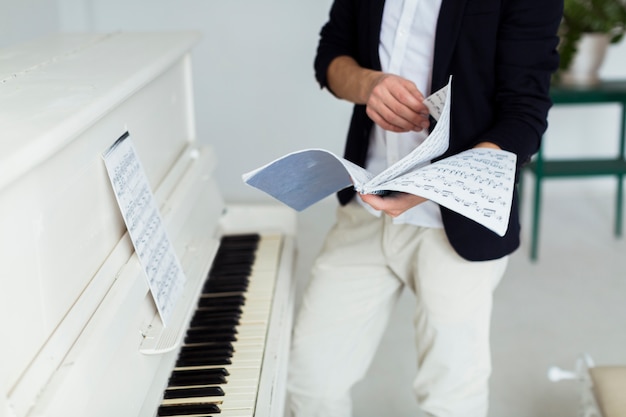 Mid sectie van de mens de bladzijden van de muzikale platen in de buurt van de vleugel