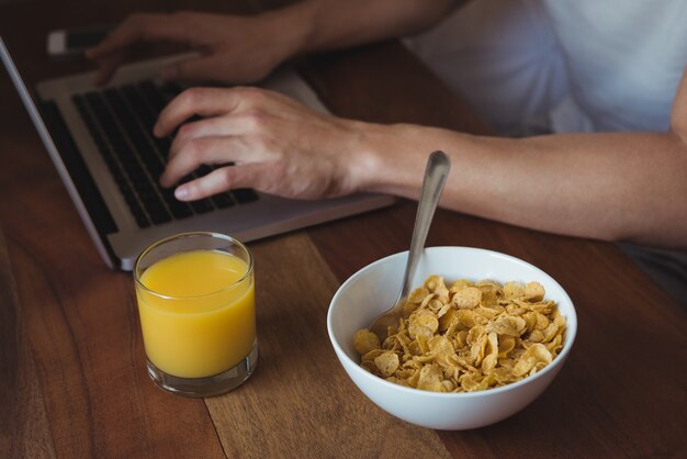 Mid sectie van man met behulp van laptop tijdens het ontbijt in de slaapkamer