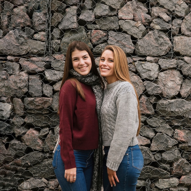 Middel van twee glimlachende vrouwen voor steenmuur die wordt geschoten