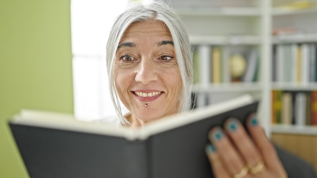 Gratis foto middelbare leeftijd grijsharige studente leesboek glimlachend aan de universiteit van de bibliotheek